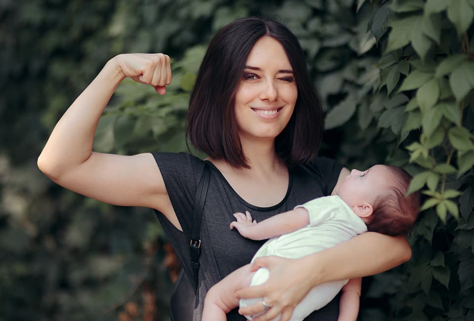 Mutter mit Baby im Arm zeigt ihre Muskeln
